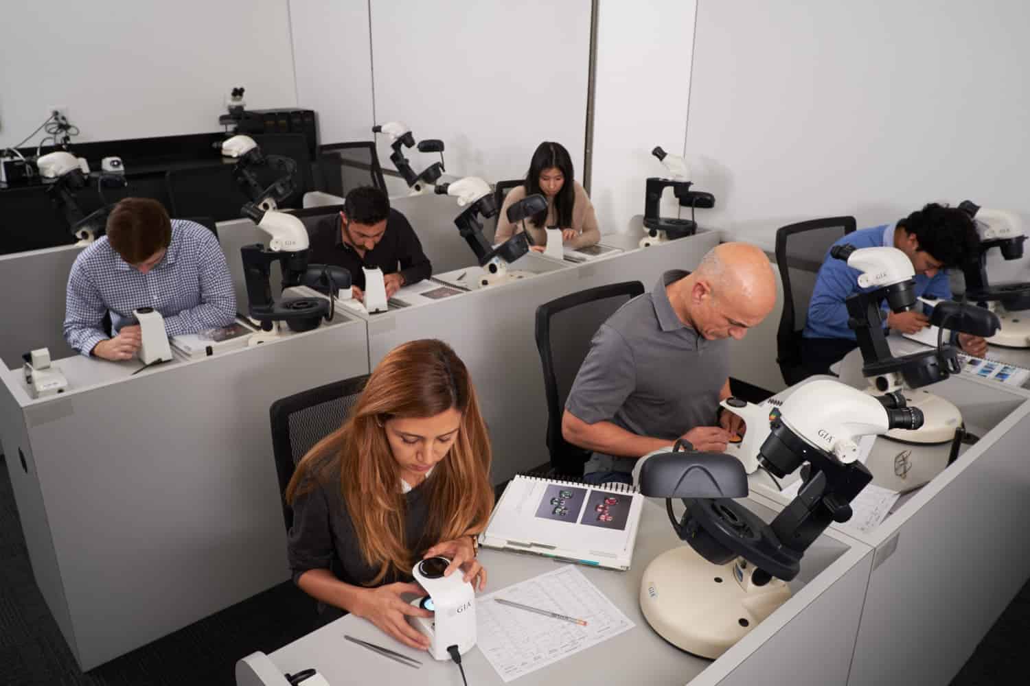 Gemology students in a classroom examining gems with microscopes.